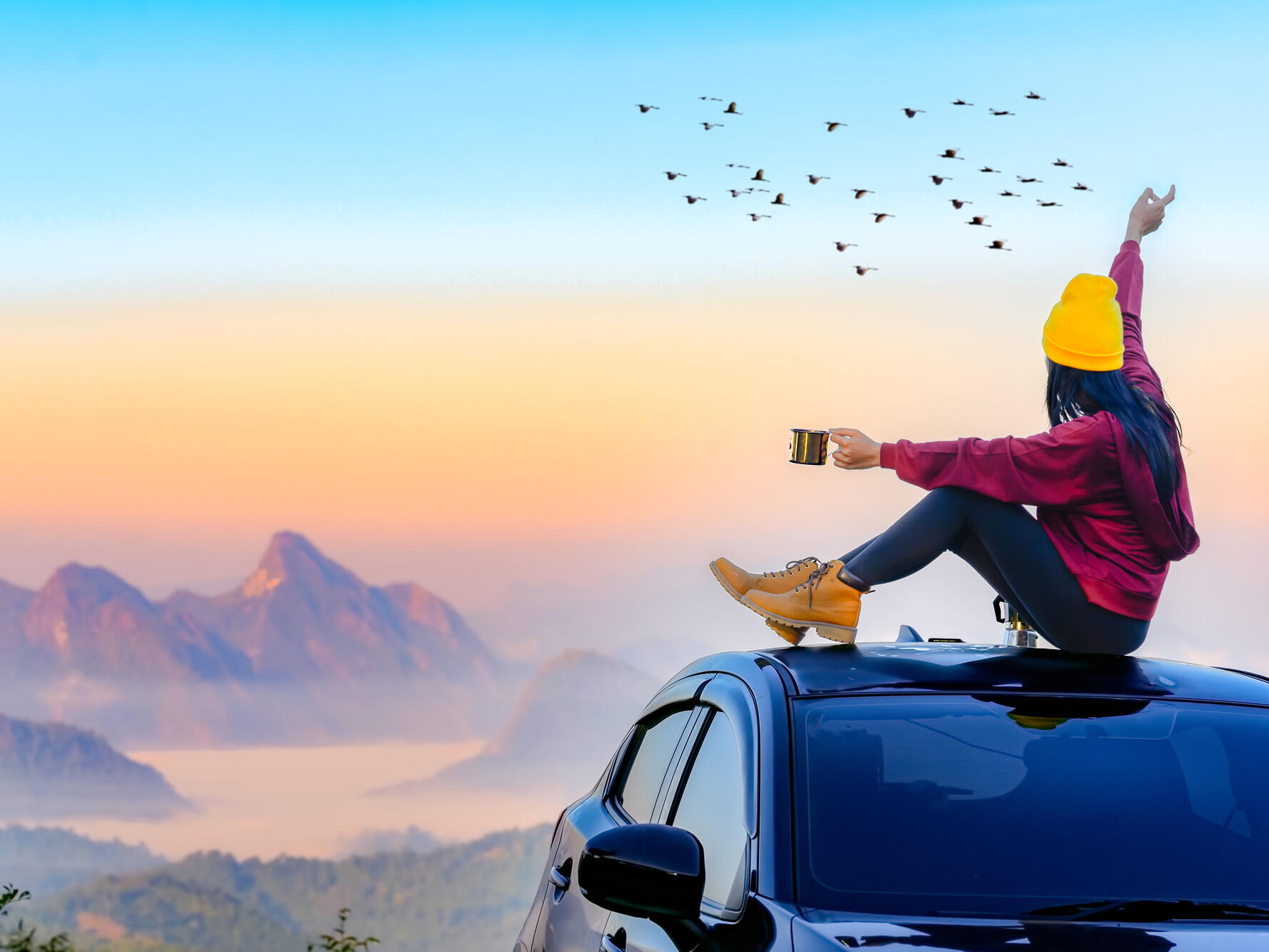 A lady sitting on a roof of a car enjoying the the view while drinking tea/coffee
