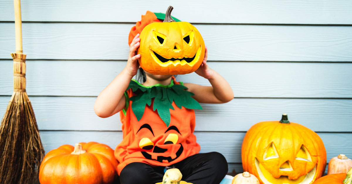 little kid in pumpkin costume holding up pumpkin