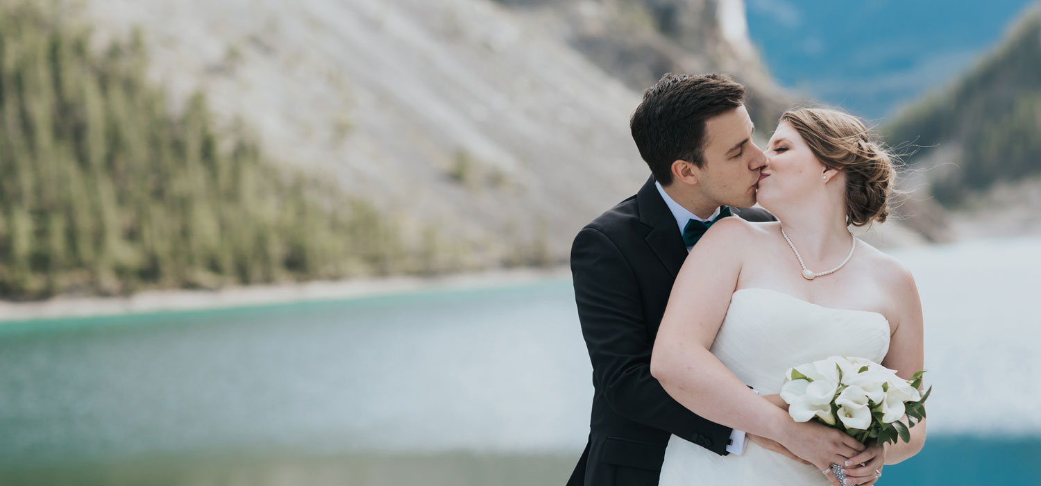 couple kissing on their wedding day in front of canmore lake