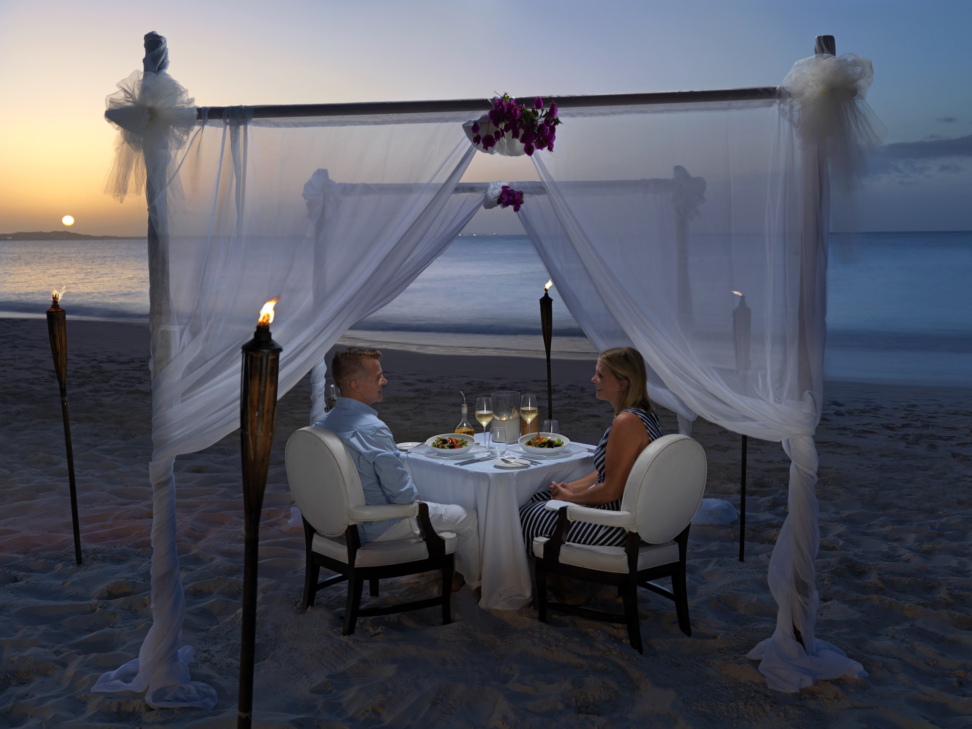 A couple dining by a beach at The Somerset on Grace Bay